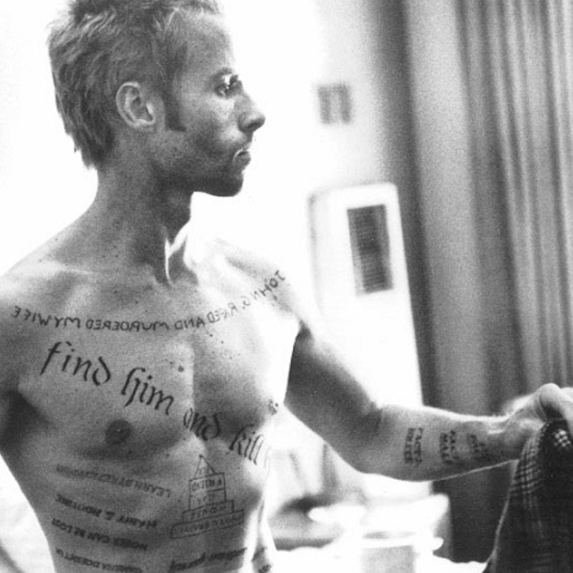 Guy Pierce as Leonard Shelby featuring a number of text-based tattoos on his torso and arms