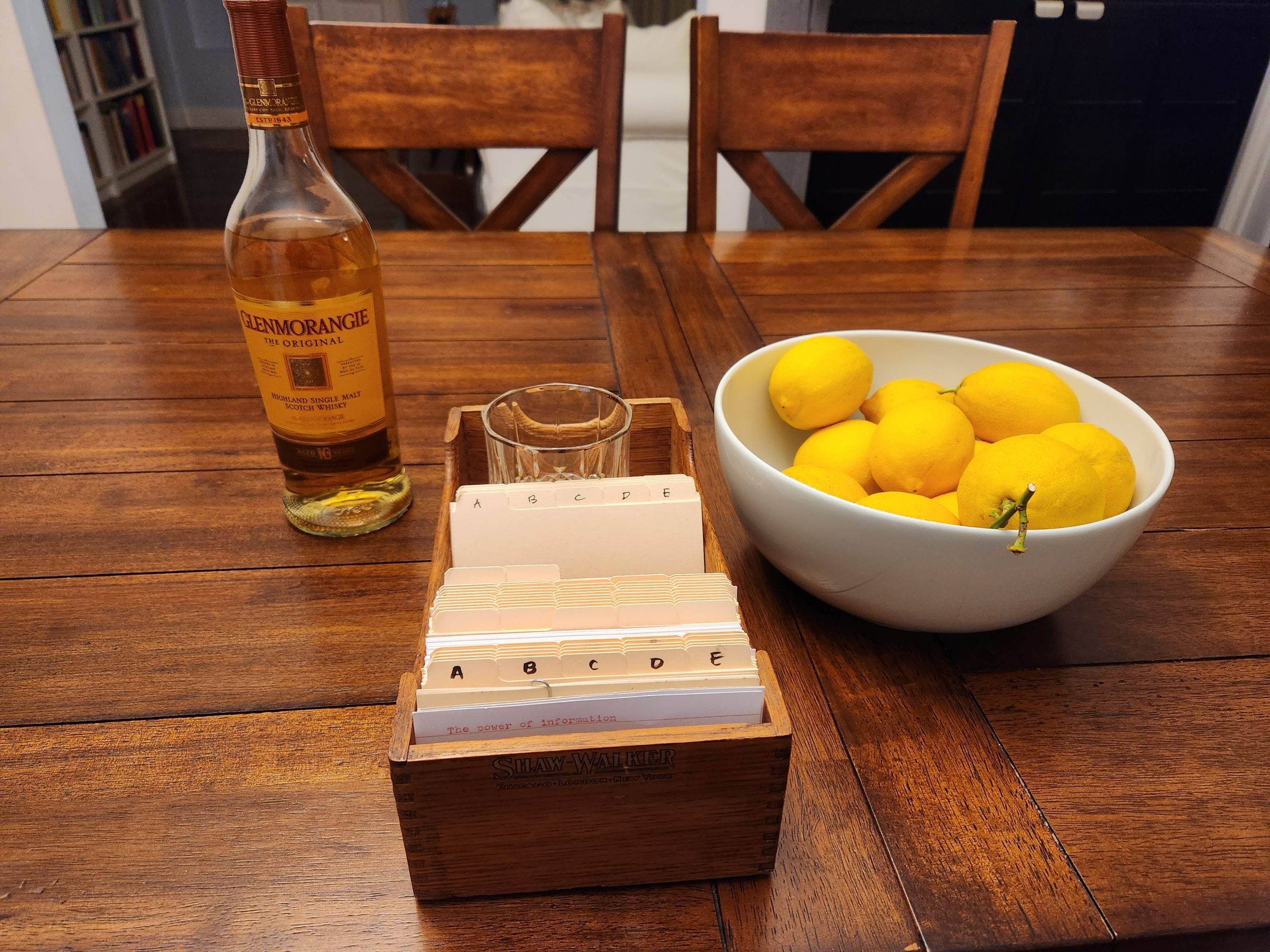 A crystal old fashioned glass serves as a following block to some index cards and card dividers in a Shaw-Walker card index box (zettelkasten). On the table next to the index are a fifth of Scotch (Glenmorangie) and a bowl of lemons.