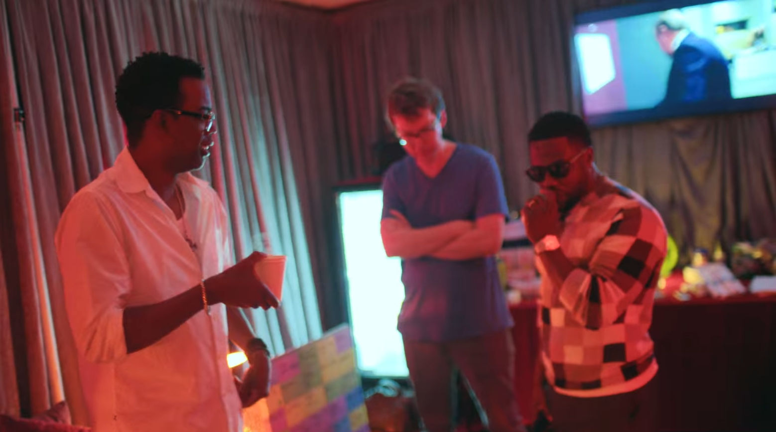 Chris Rock and Kevin Hart standing up in a green room. Behind them is a small board covered with rainbow colored slips of paper.