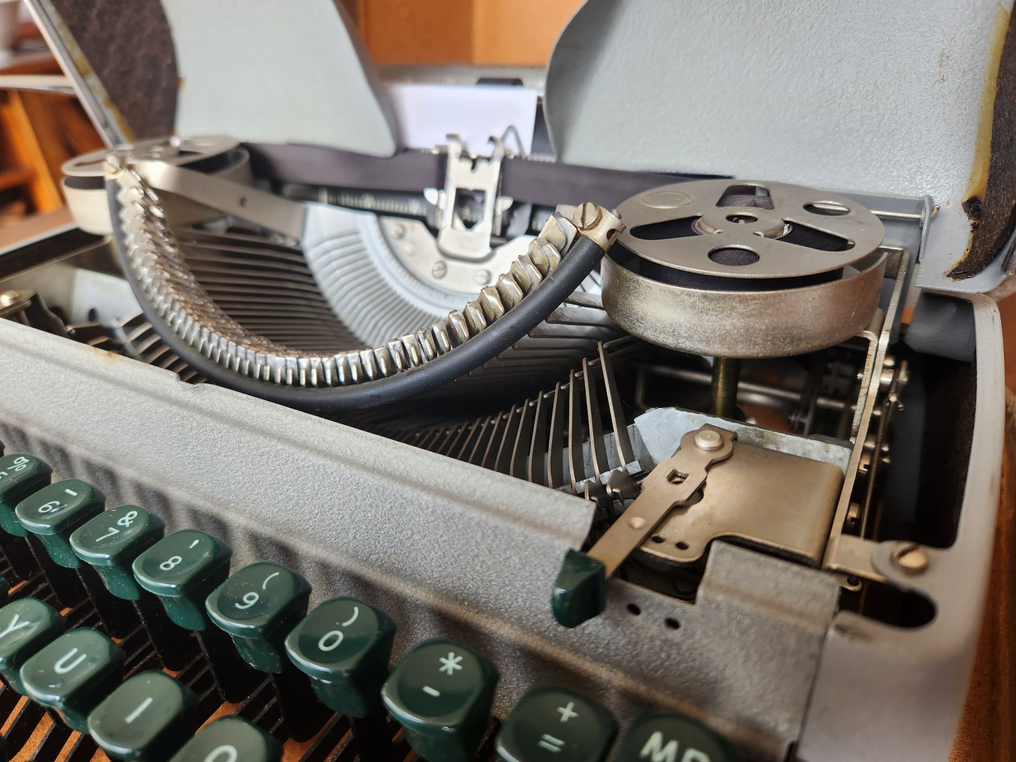 The open hood of the typewriter featuring the right ribbon spool in front of which is the color selector for either the top color, the bottom color or the stencil setting (middle).