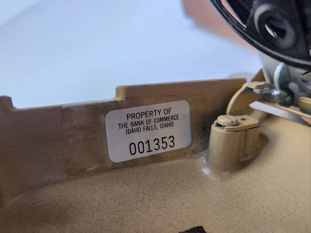 View of a silver property tag found underneath the hood of a 1961 Royal FP typewriter indicating it's property of the Bank of Commerce in Idaho Falls.