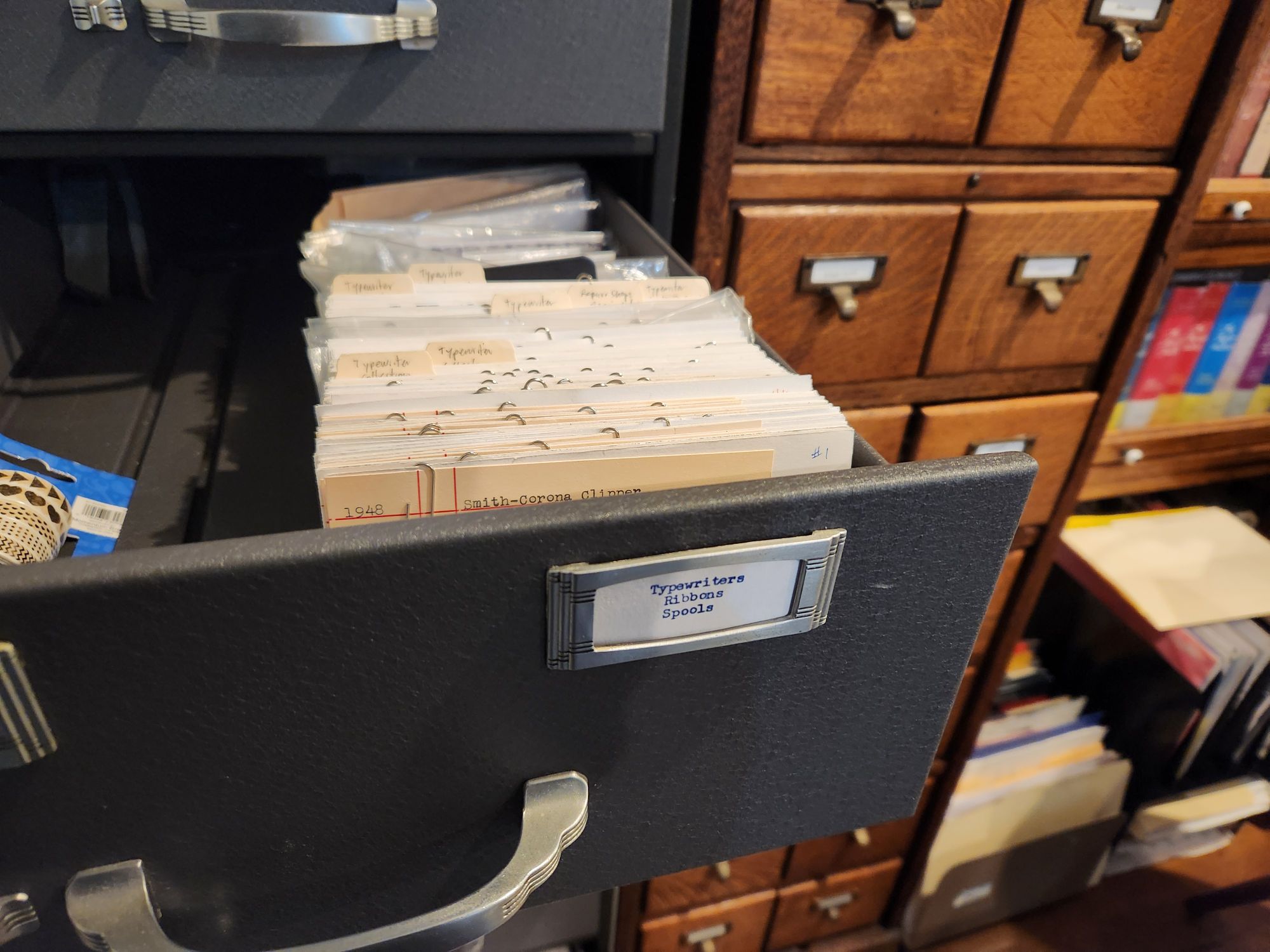 View into the drawer of a metal index card filing cabinet full of tabbed cards and index cards. The section is labeled 'Typewriters / Ribbons / Spools' and the tabs are all typewriter related.