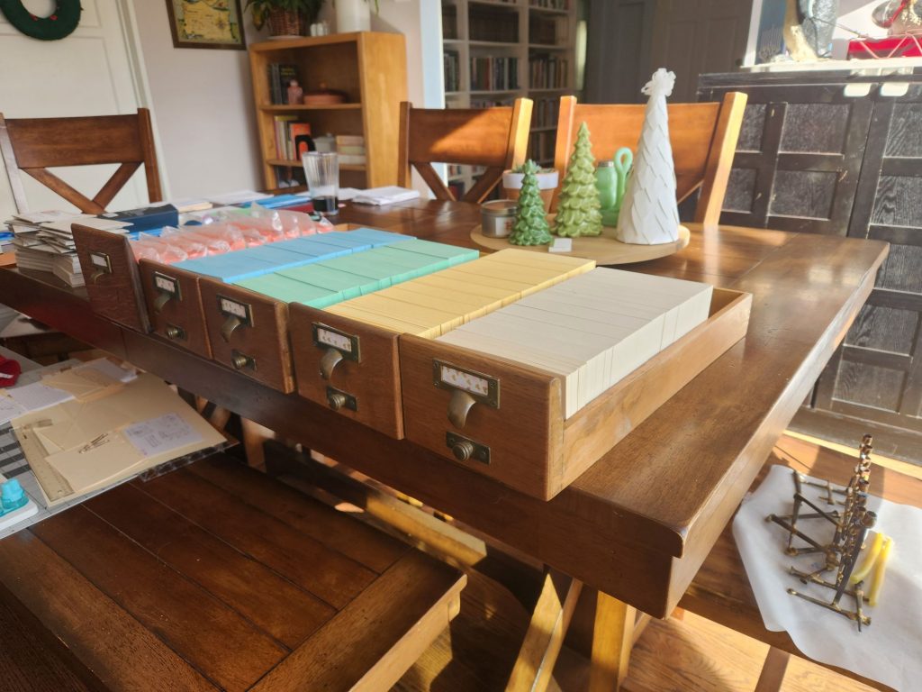 Five card catalog drawers lined up and full of ivory, buff, green, blue, and salmon index cards