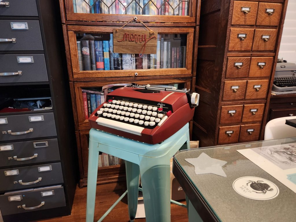 1964 Sears Cutlass sitting at an angle on a sea green metal bar stool in front of a barrister bookcase flanked by card index filing cabinets.