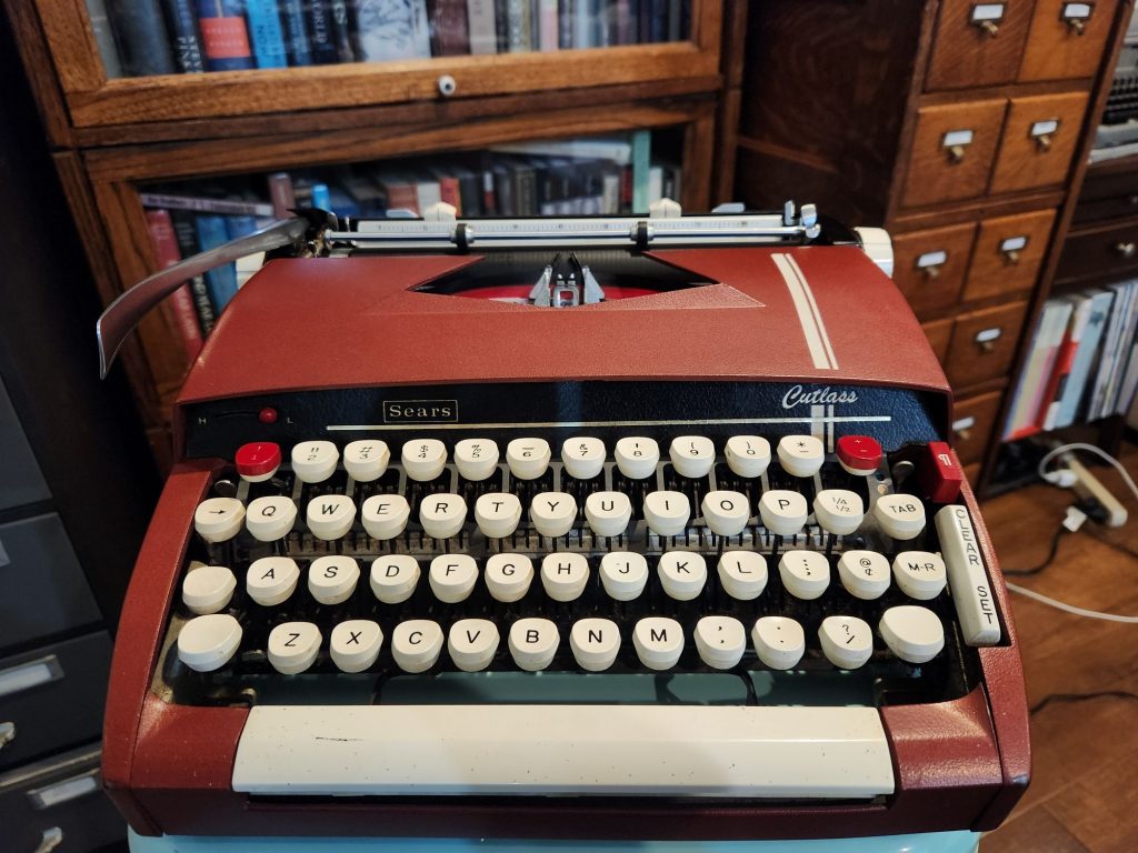 Close up angled from the top of a burgundy 1964 Sears Cutlass which has a pair of racing strips on the right side of the hood.