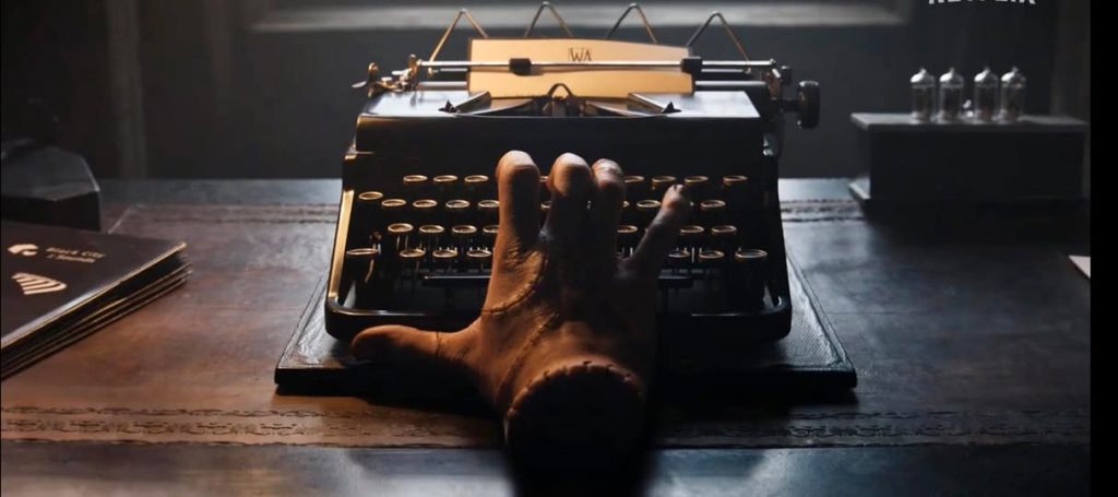 Thing, a disembodied hand, types on a black portable Juwel 3 typewriter.