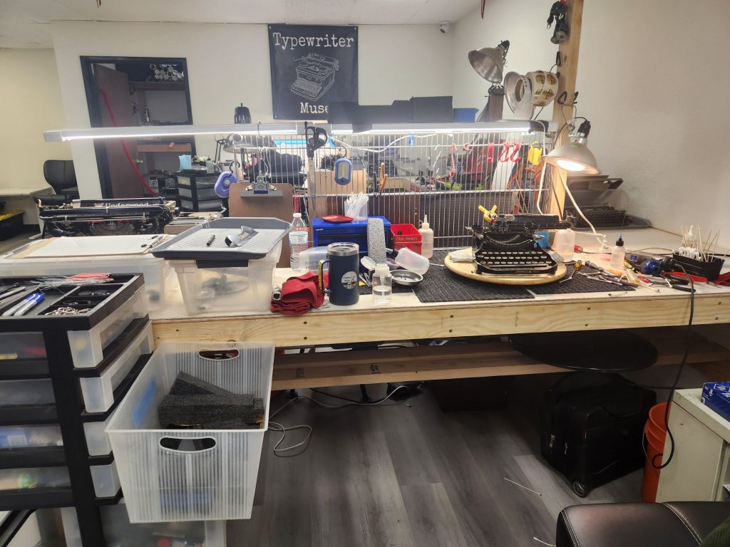 A typewriter mechanic's bench with a variety of tools on it and a lazy susan with a typewriter on it for restoration