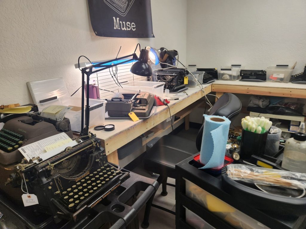 Typewriter repair bench at Typewriter Muse with a typewriter surrounded by tools and an anglepoise lamp.