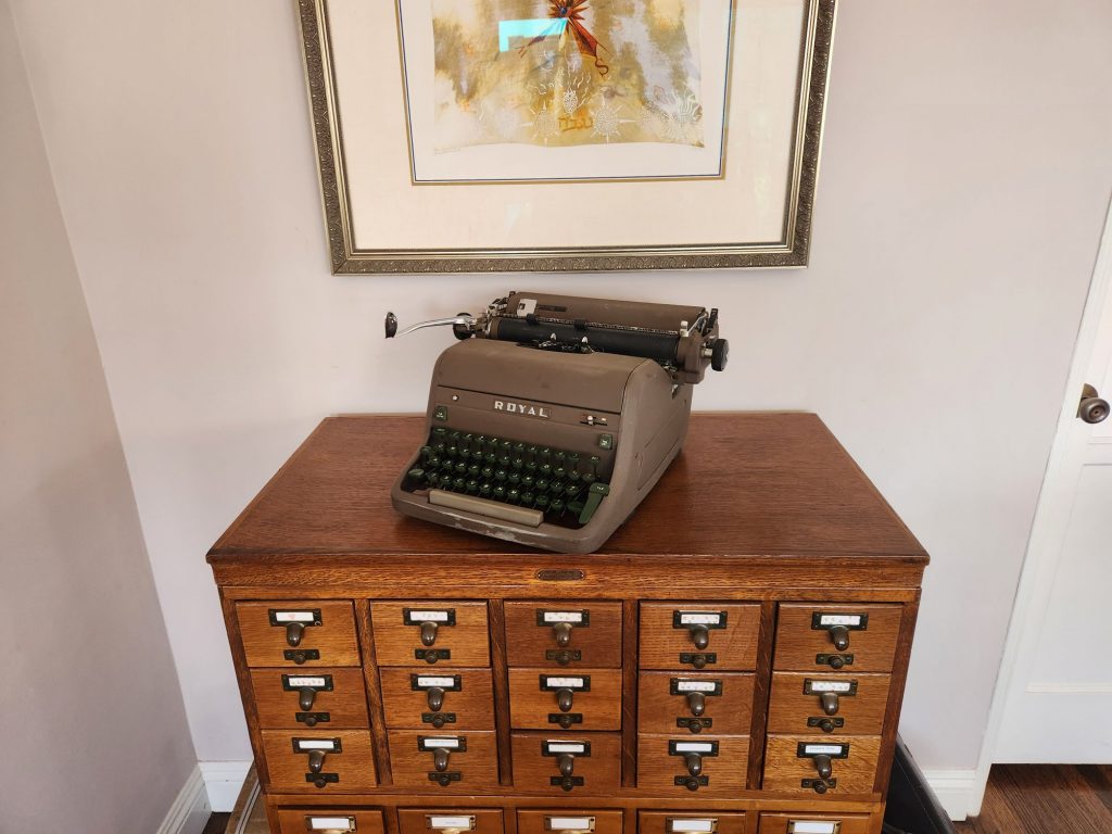 A brown crinkle painted 1954 Royal HH typewriter with green keys sits on an oak library card catalog file.