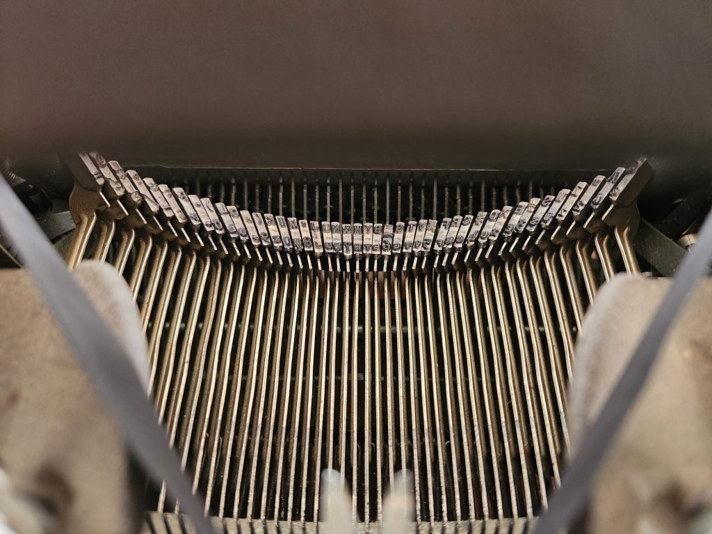 View through the hood of a Royal HH typewriter onto the entirety of the segment featuring all the slugs on of a san-serif Royal Pica Double Gothic typeface