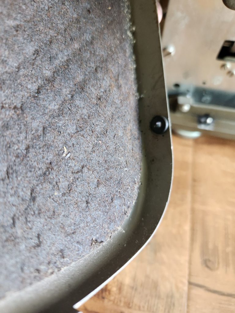 Interior of brown crinkle painted Remington standard typewriter side panel with a new black rubber grommet inserted perfectly into the hole on its bottom.