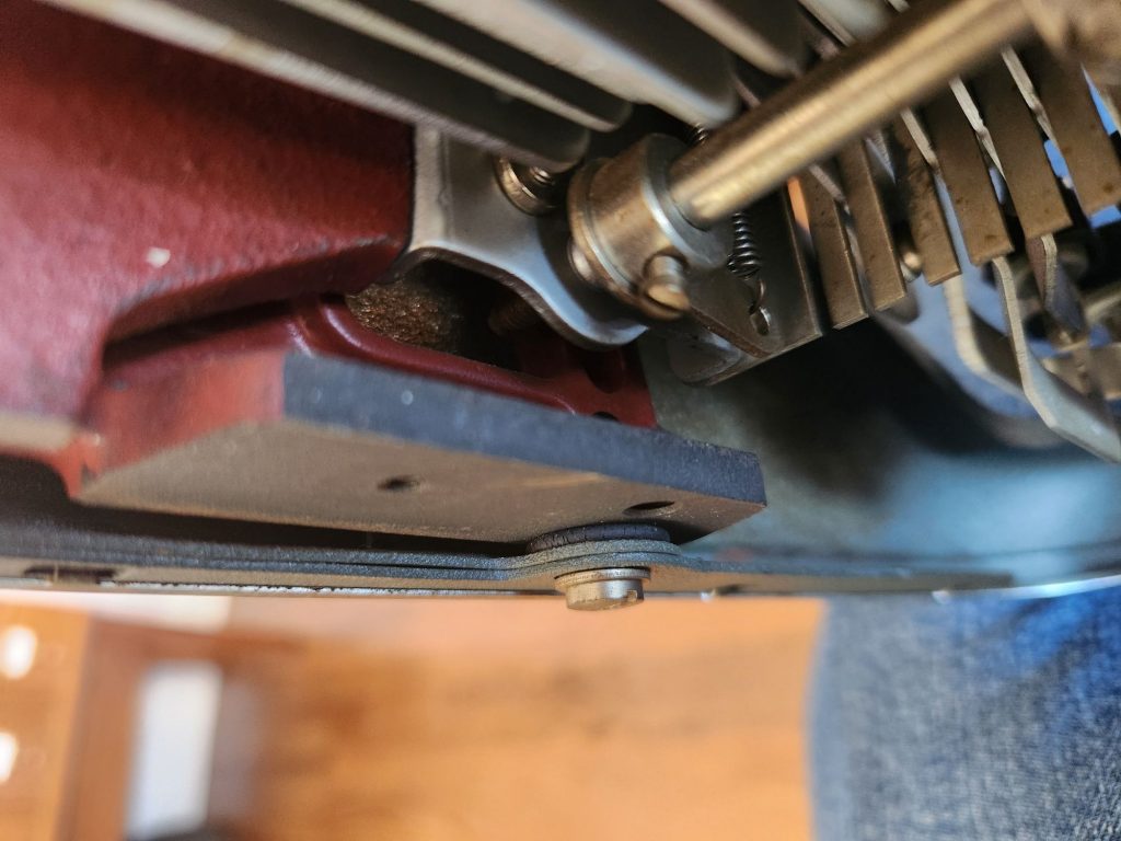View of the back corner underneath an Olympia SG1 typewriter featuring a crushed rubber washer between the body shell and the solid steel chassis of the typewriter. It look like it's less than a millimeter thick.
