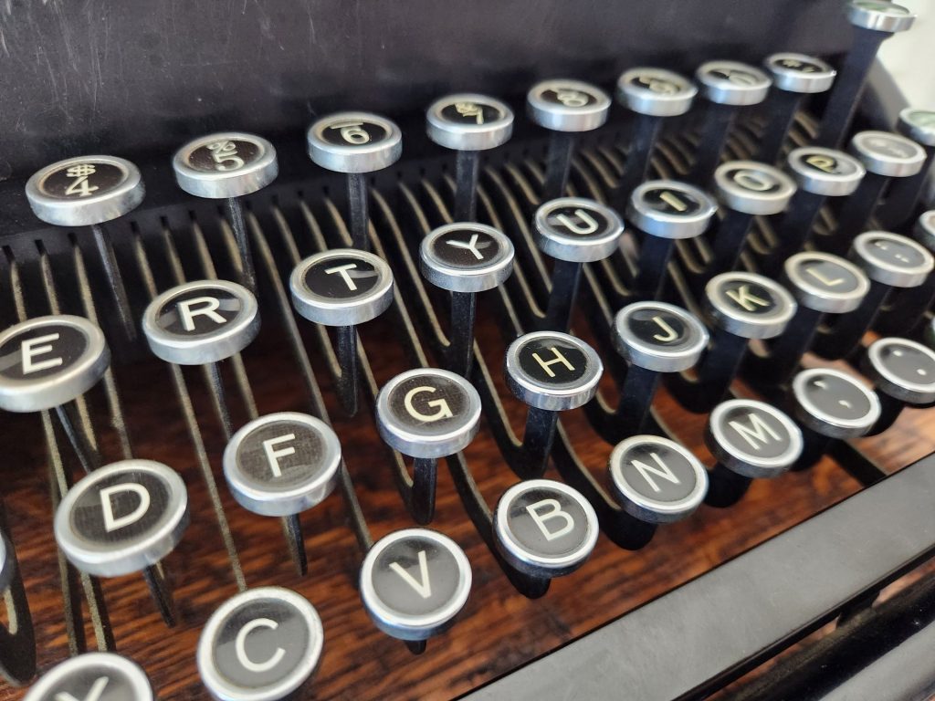 An angle on the keyboard of a Woodstock typewriter keyboard. The silver keyrings and glass top keys gleam without any tarnish.