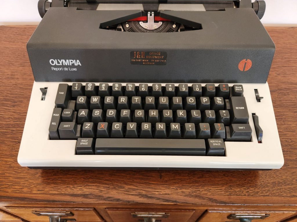 Close up view of the keyboard of a Olympia Report de Luxe typewriter. Several of the keys like the x, -, and / are in red to indicate that they auto-repeat.