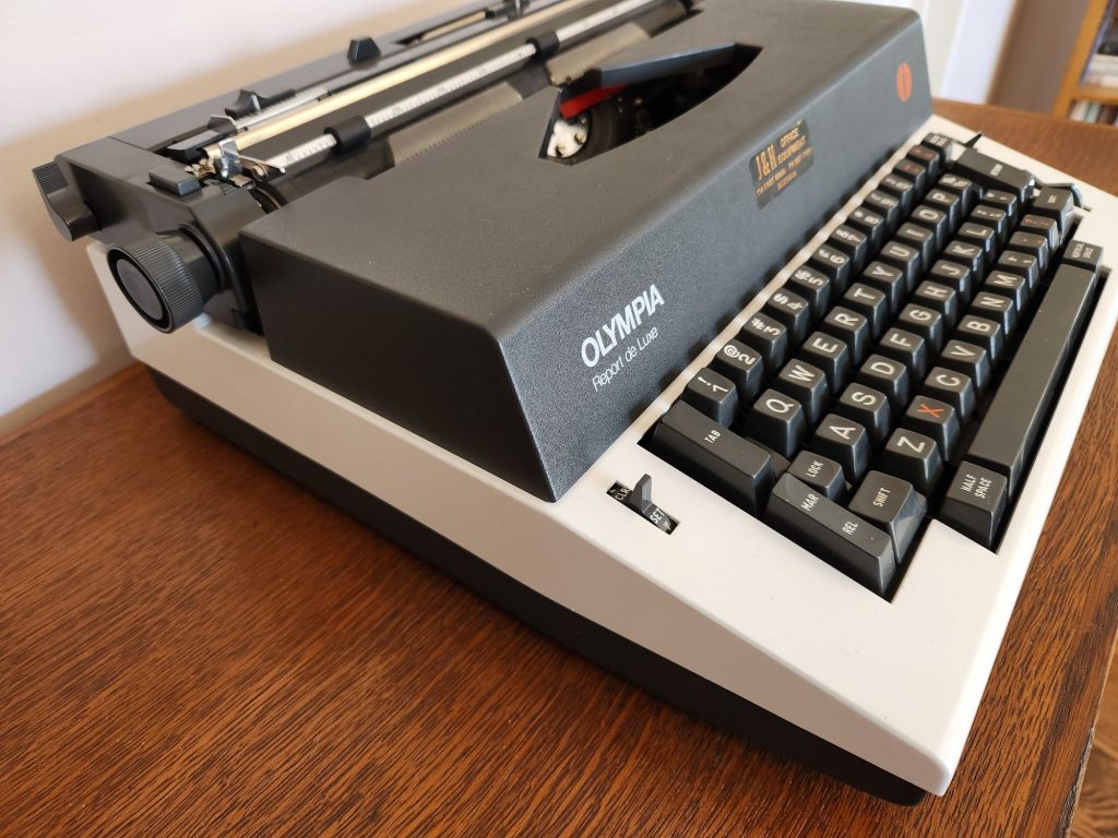 Oblique view from the left side of a Olympia Report de Luxe typewriter. In the front left corner of the keyboard is a switch for setting and clearing tabs.