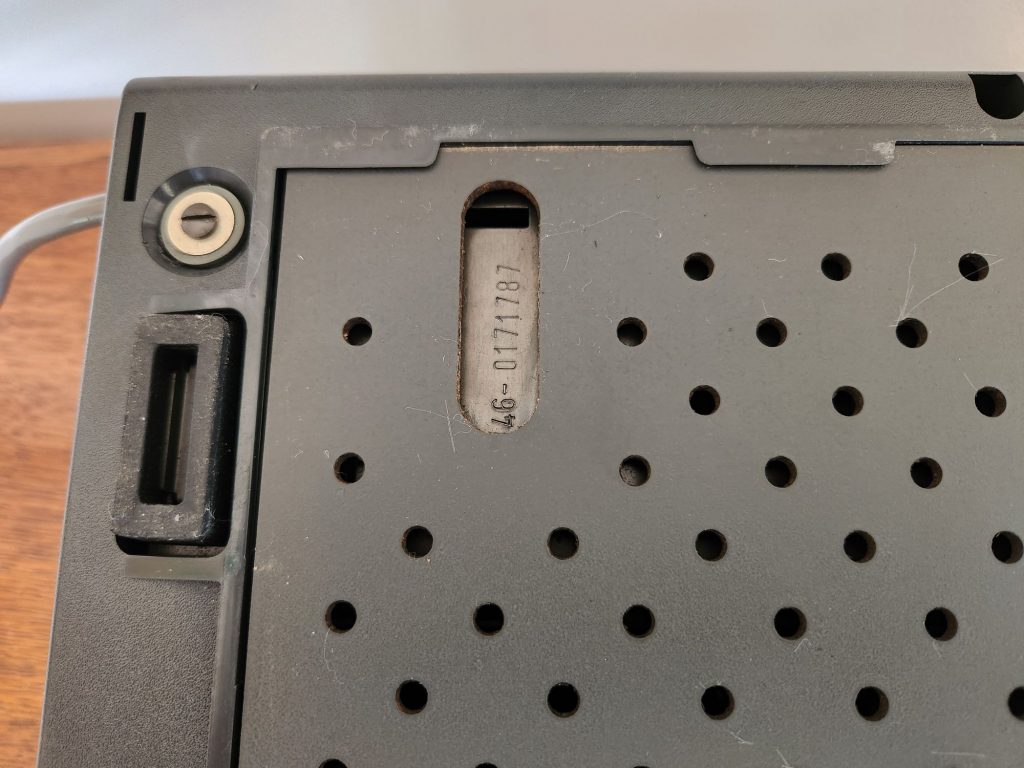 A small window in the bottom of the Olympia Report de Luxe typewriter shows the serial number stamped on the metal chassis beneath the plastic cover.