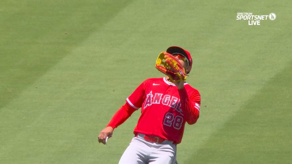 Siri with an index card in his right hand raises his glove in his left hand for a one-handed catch in center field