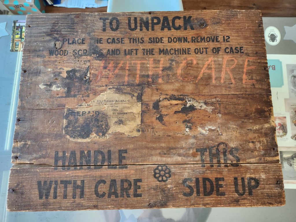 A view down onto the top of a stained an patina covered Woodstock Typewriter Crate which has a shipping label stained and mostly peeled off.