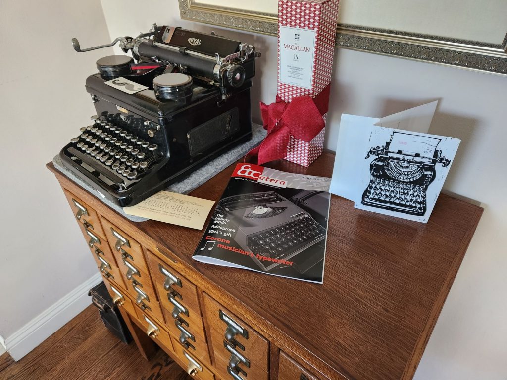 Spring 2026 issue of Etcetera magazine on a library card catalog next to a Royal KHM and a gift bottle of scotch.
