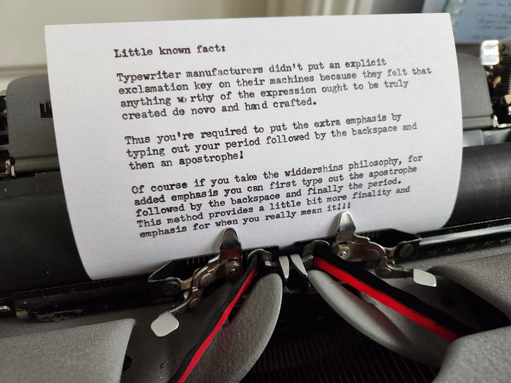 Typed 4 x 6" index card in the carriage of a grey typewriter with black/red ribbon. The card reads: "Little known fact: Typewriter manufacturers didnt put an explicit exclamation key on their machines because they felt that anything worth of the expression ought to be truly created de novo and hand crafted.  Thus you're required to put the extra emphasis by typing out your period followed by the backspace and then an apostrophe!  Of course if you take the widdershins philosophy, for added emphasis you can first type out the apostrophe followed by the backspace and finally the period. This method provides a little bit more finality and emphasis for when you really mean it!!!