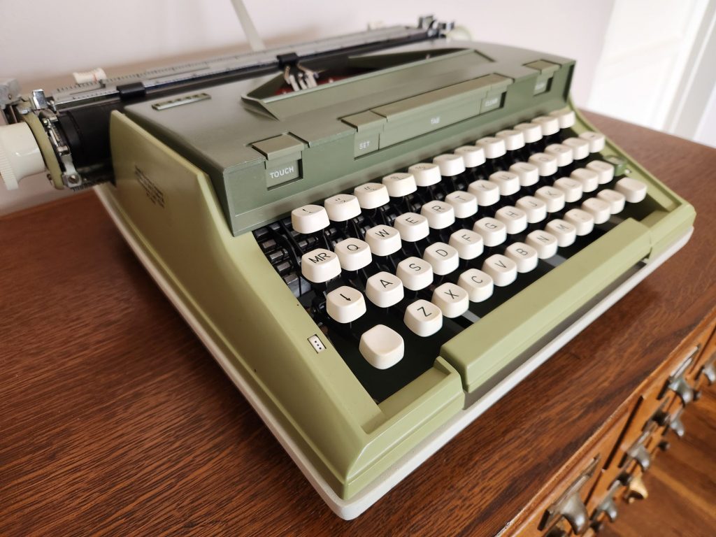 oblique angle onto the front left corner of a Sears Newport typewriter there's a button on the corner of the hood that reads "TOUCH"
