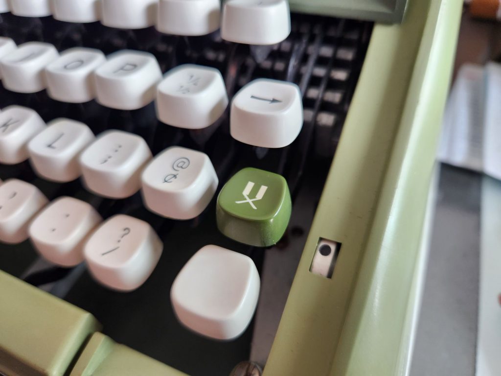 Close up of the right side of an avocado Sears Newport typewriter featuring a dark green key next to the @/¢ featuring what appears to be two typebars crossing each other