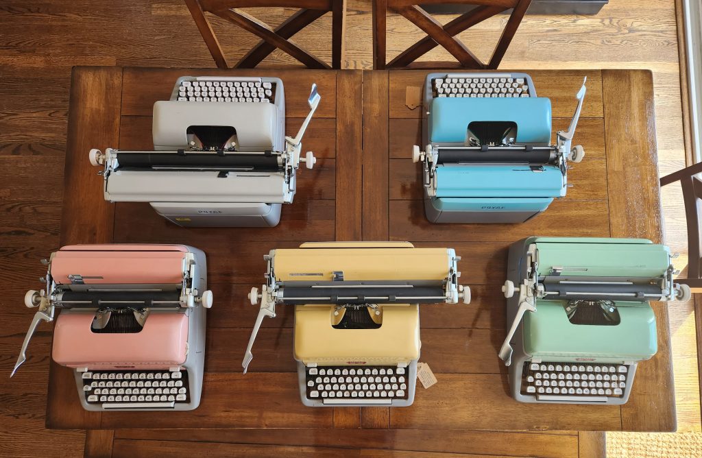 Overhead view of five Royal FP standard typewriters in pink, yellow, green, blue, and a pearl-gray.