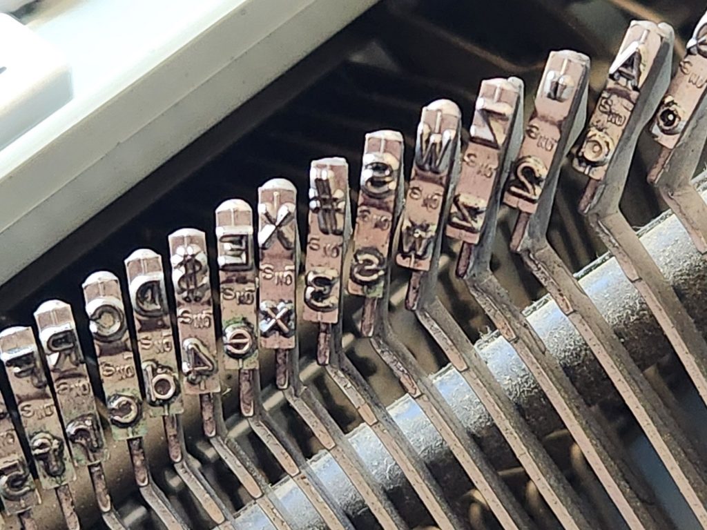 Close up of the slugs on the left hand side of a 1971 Hermes 3000 featuring a san serif Epoca typeface. The foundry mark on the slugs is "S NO".