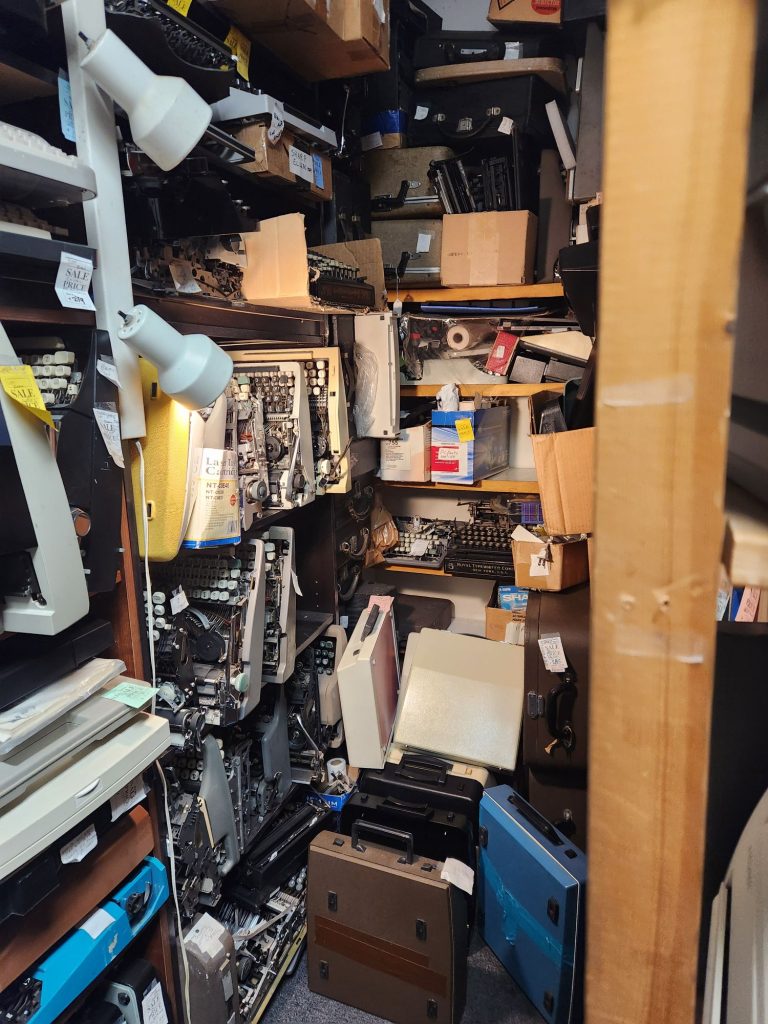 Several dozens of parts typewriters packed into shelves in a dark corner of a typewriter shop.
