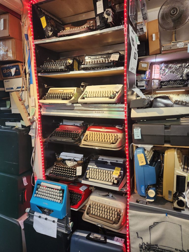 A display case with a dozen portable typewriters in various shapes and colors.