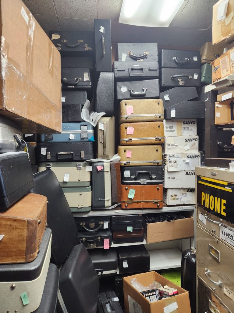 A corner of a typewriter shop with more than 36 portable typewriter cases stacked up and filling the entire frame.
