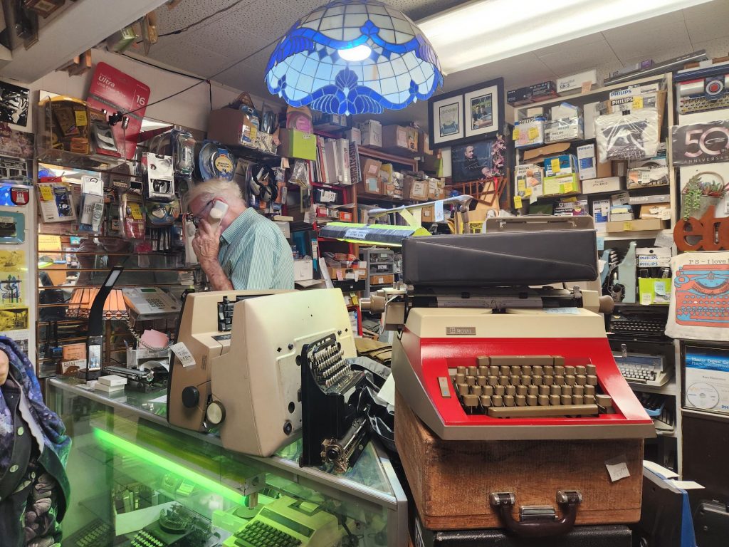 Helmut Schuze on the phone in the front of his typewriter shop literally stuffed with machines and typewriter paraphernalia.