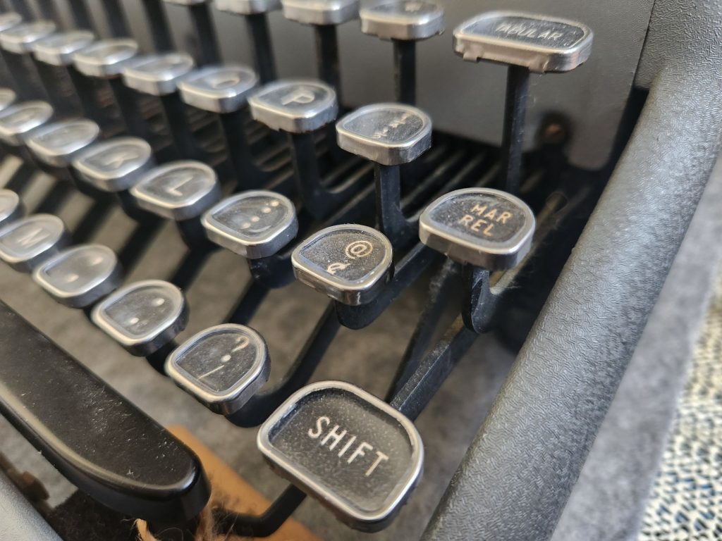 Angle on a typewriter keyboard with glass tombstone keys. In the front, we're focused on the @ key.